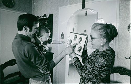 Реколта снимка на бащата с детето си показва снимка baby39 в рамка, която държи на баба.- Декември 1970